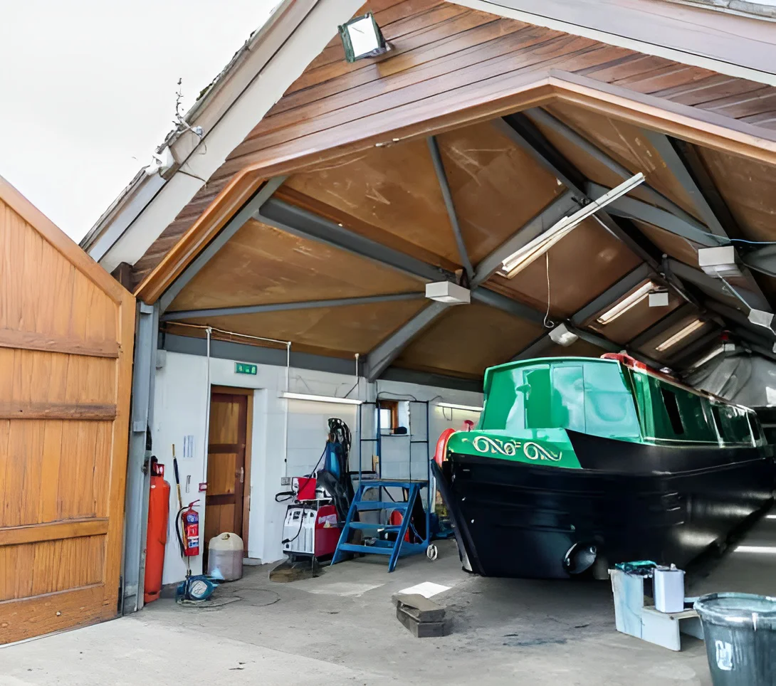 A green and black narrowboat inside the Keel Boat Services workshop, with welding equipment beside it